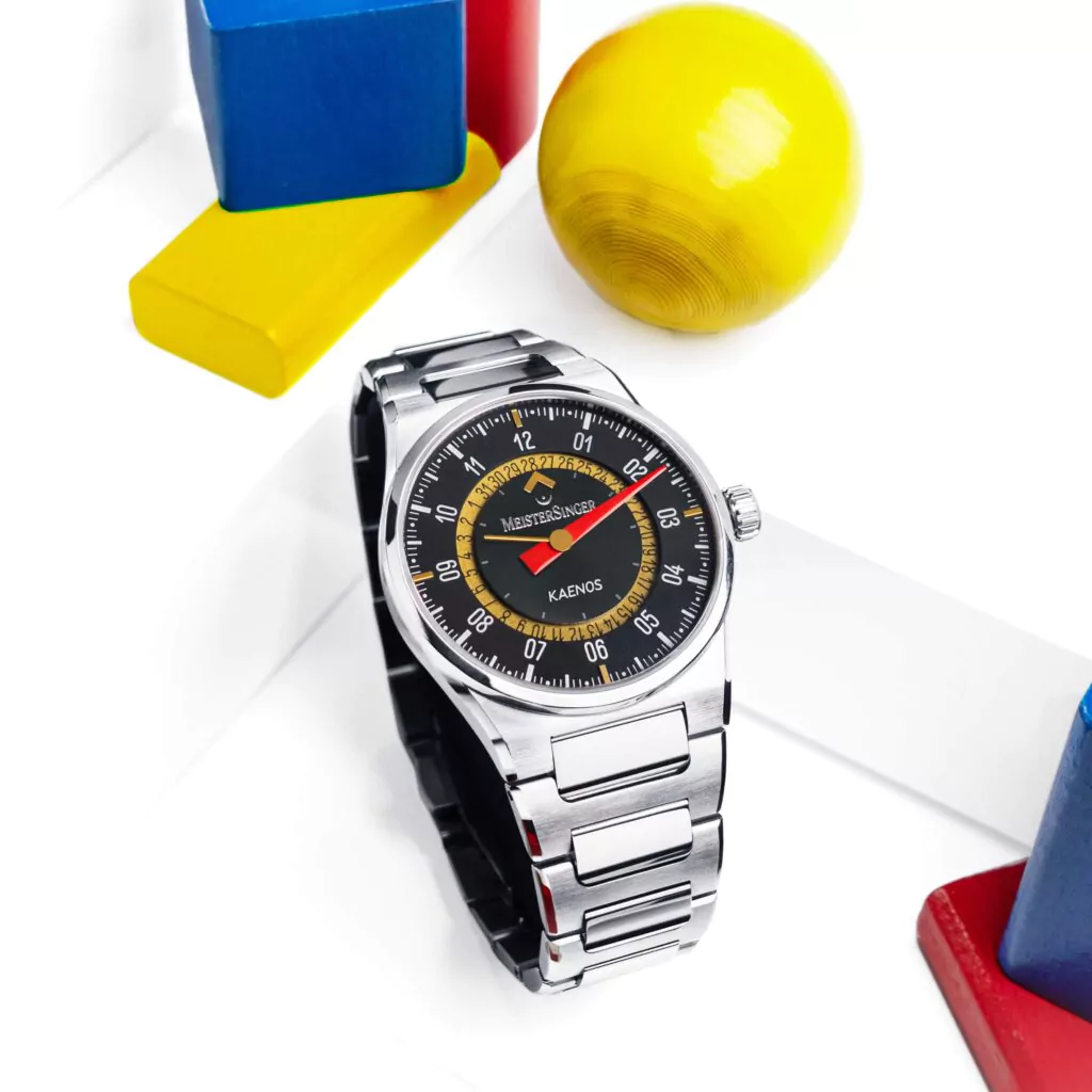 MeisterSingerとAlain Silbersteinのコラボレーションモデル Kaenos Open Date（ED-KSOD-AS2025）の製品画像。カラフルなインデックスと12時位置のオープンデイト構造を横構図で捉えたスチールカット。